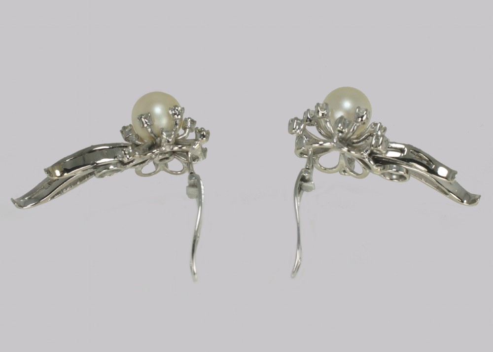 A pair of 1950s 18ct white gold clip-on earrings featuring central cultured pearls surrounded by diamond-set floral sprays and sweeping curved accents. View IV