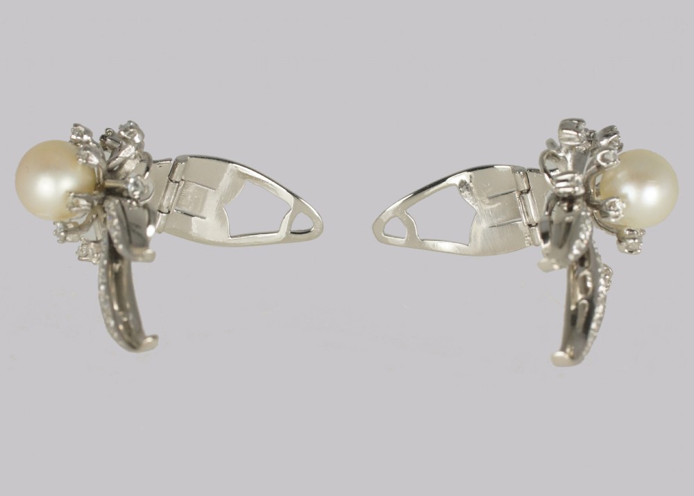 A pair of 1950s 18ct white gold clip-on earrings featuring central cultured pearls surrounded by diamond-set floral sprays and sweeping curved accents. View V