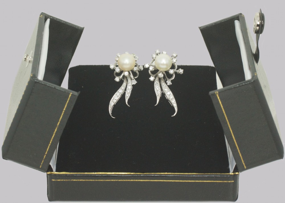 A pair of 1950s 18ct white gold clip-on earrings featuring central cultured pearls surrounded by diamond-set floral sprays and sweeping curved accents. View VI
