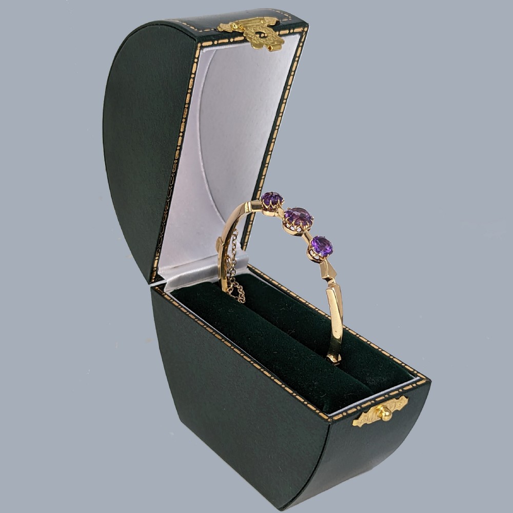 An 18ct yellow gold Victorian hinged bangle featuring three claw-set round purple amethysts and an attached safety chain. View III