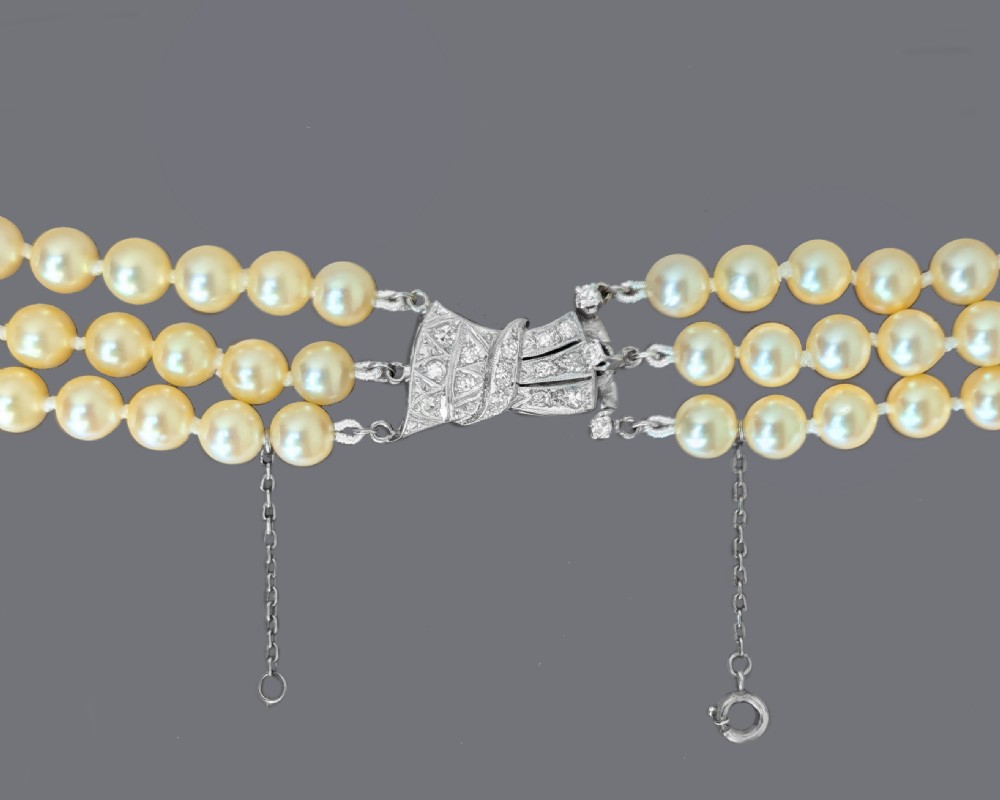 A 1950s triple strand cream pearl necklace featuring an 18ct white gold bow clasp set with brilliant diamonds. View VII