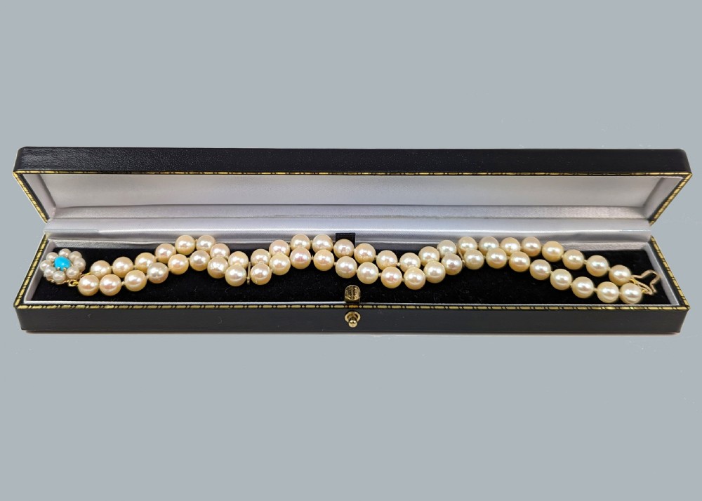 A vintage double strand pearl bracelet featuring cream pearls connected by a 9ct yellow gold clasp with a central turquoise stone surrounded by seed pearls. View VI