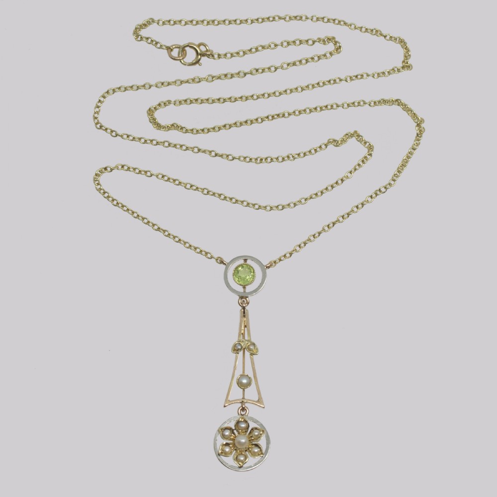 An Edwardian gold and platinum pendant featuring a circular peridot top setting and an openwork geometric drop with seed pearls and a floral motif. View II