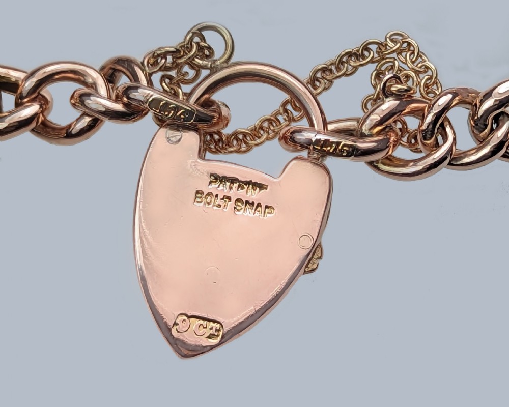 A Victorian 9ct yellow gold knot link chain bracelet featuring embedded rubies and seed pearls, secured by a heart-shaped padlock clasp with a safety chain. View IV