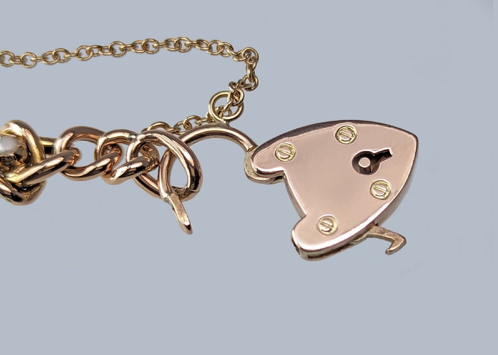 A Victorian 9ct yellow gold knot link chain bracelet featuring embedded rubies and seed pearls, secured by a heart-shaped padlock clasp with a safety chain. View VII