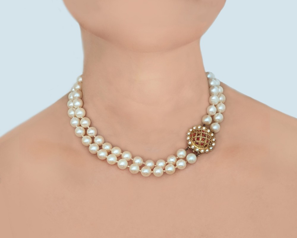 A two-strand cream cultured pearl necklace featuring an ornate circular 9ct gold clasp embellished with garnets and seed pearls. View IV