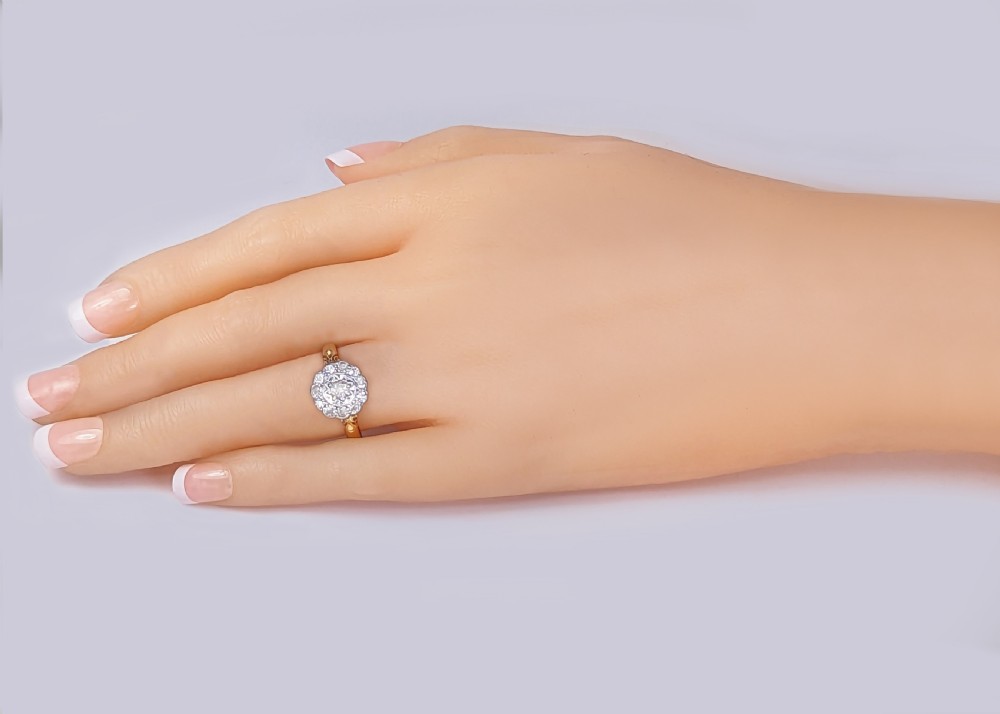 An Edwardian cluster ring with a central old cut diamond surrounded by smaller accent diamonds in a circular setting, set on an 18ct yellow gold band with carved shoulders. View XII