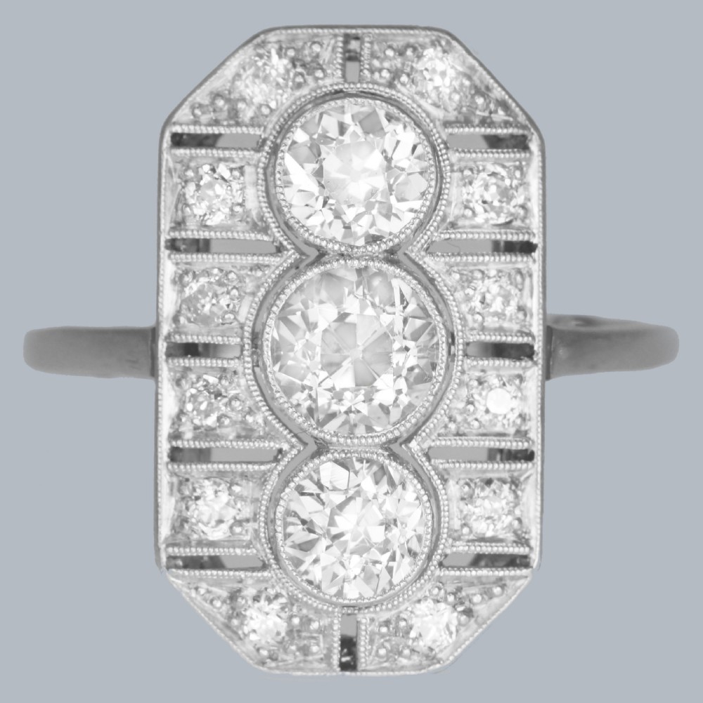 An Art Deco platinum plaque ring featuring three central old European cut diamonds framed by geometric milgrain borders and accent diamonds.