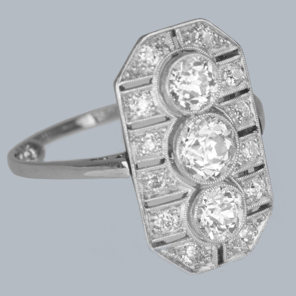 An Art Deco platinum plaque ring featuring three central old European cut diamonds framed by geometric milgrain borders and accent diamonds. View VII