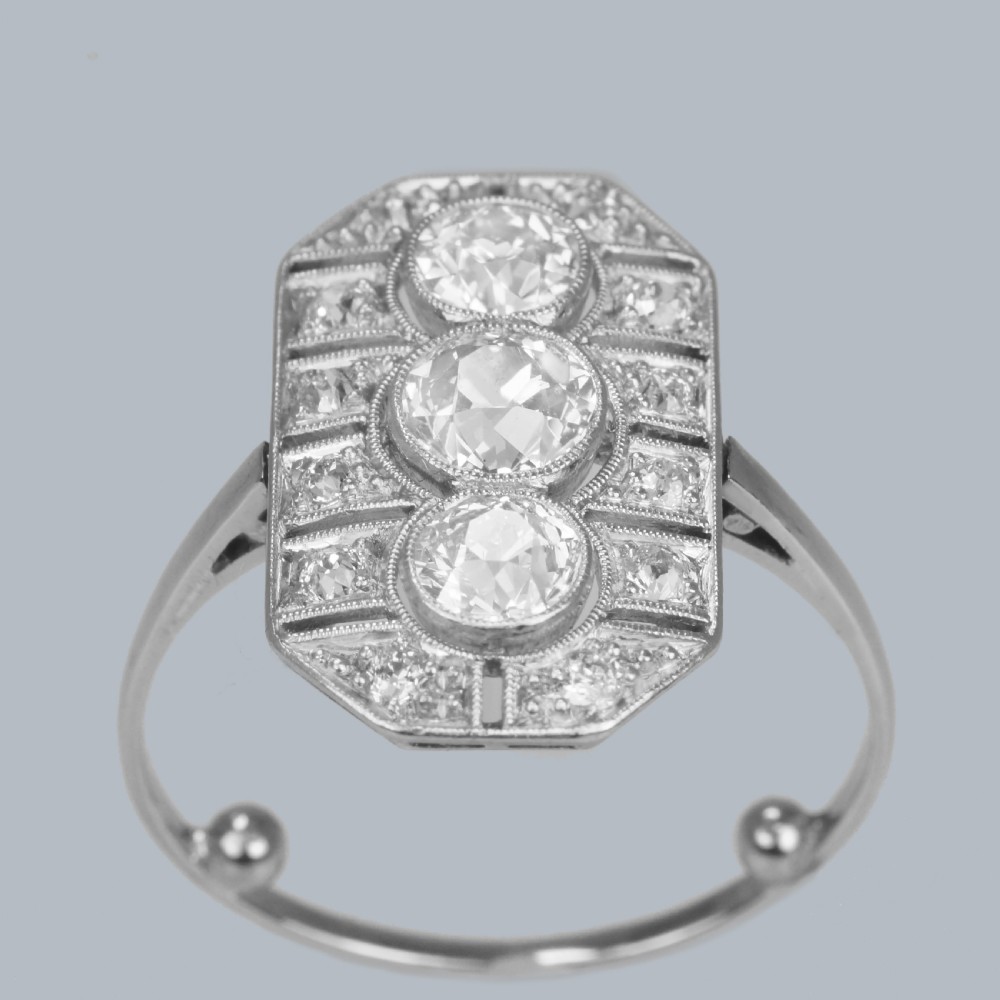 An Art Deco platinum plaque ring featuring three central old European cut diamonds framed by geometric milgrain borders and accent diamonds. View IX