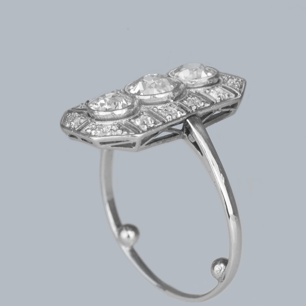 An Art Deco platinum plaque ring featuring three central old European cut diamonds framed by geometric milgrain borders and accent diamonds. View XI