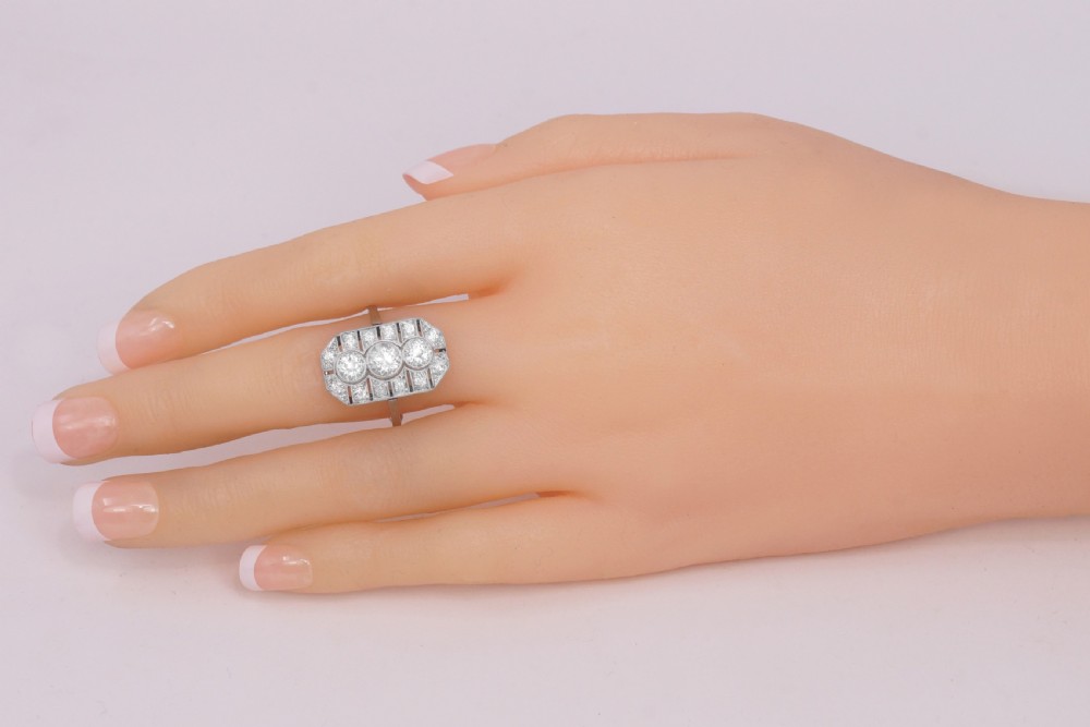 An Art Deco platinum plaque ring featuring three central old European cut diamonds framed by geometric milgrain borders and accent diamonds. View XII