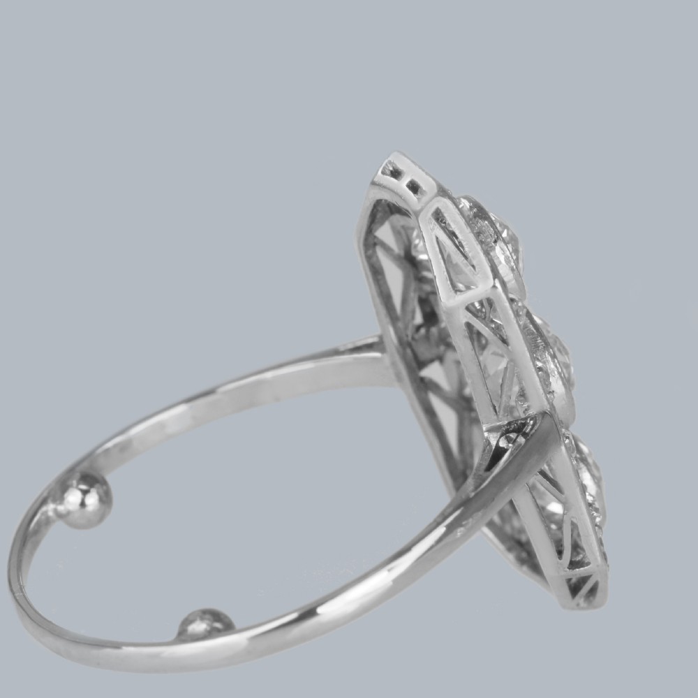 An Art Deco platinum plaque ring featuring three central old European cut diamonds framed by geometric milgrain borders and accent diamonds. View XIII