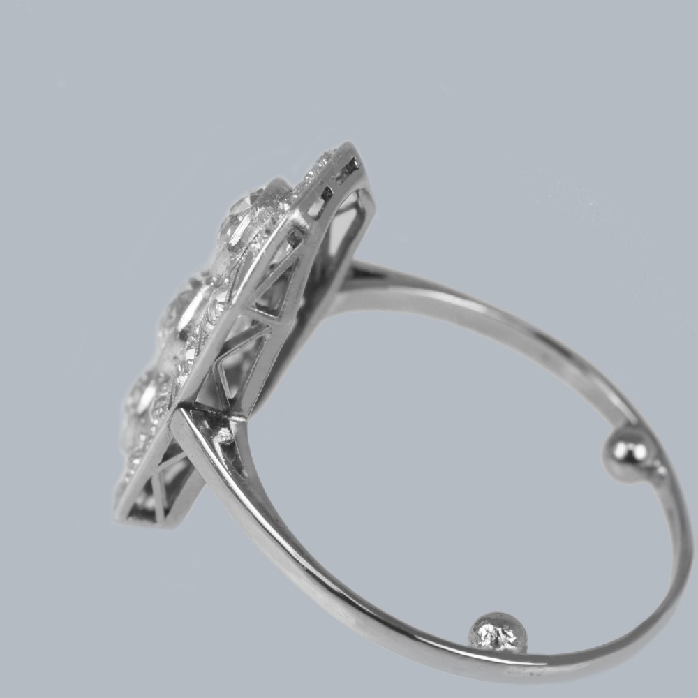 An Art Deco platinum plaque ring featuring three central old European cut diamonds framed by geometric milgrain borders and accent diamonds. View XIV