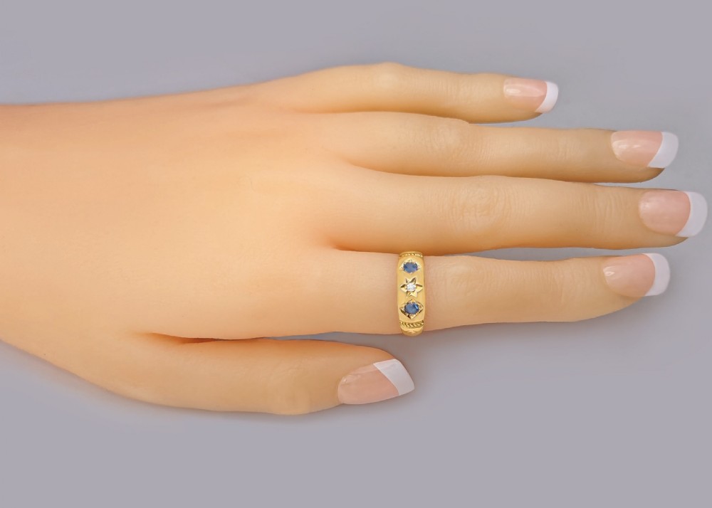 An 18ct yellow gold Victorian band featuring two oval blue sapphires flanking a central star-set diamond. View VII