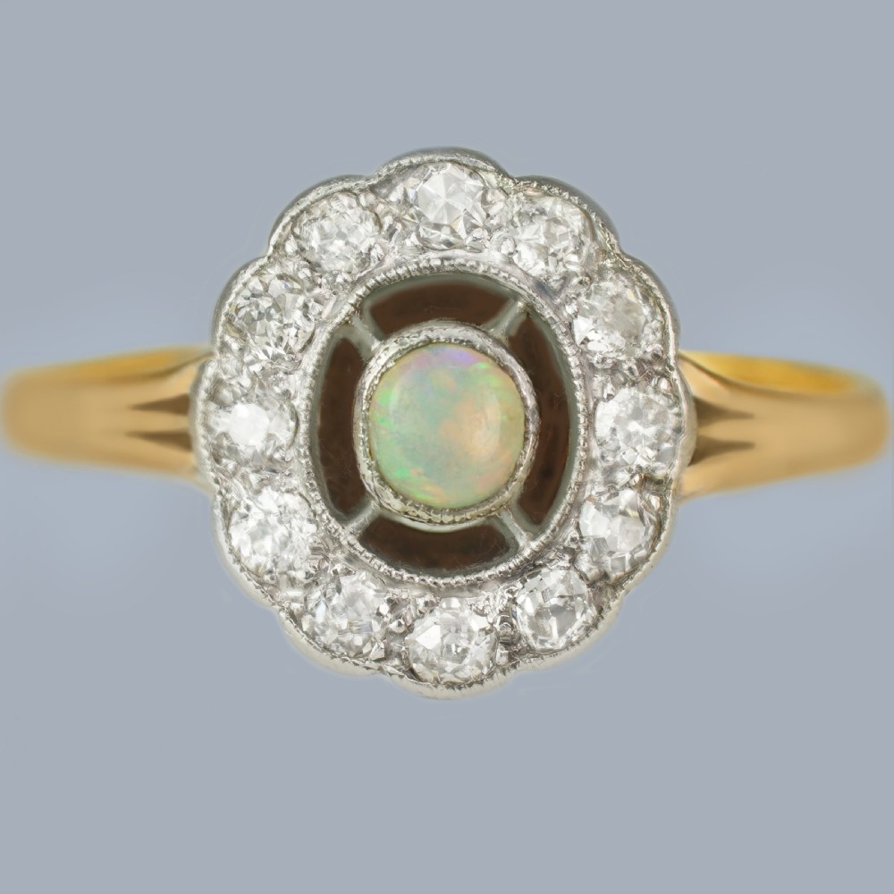 An Edwardian 18ct gold and platinum cluster ring featuring a central cabochon opal surrounded by a halo of diamonds.