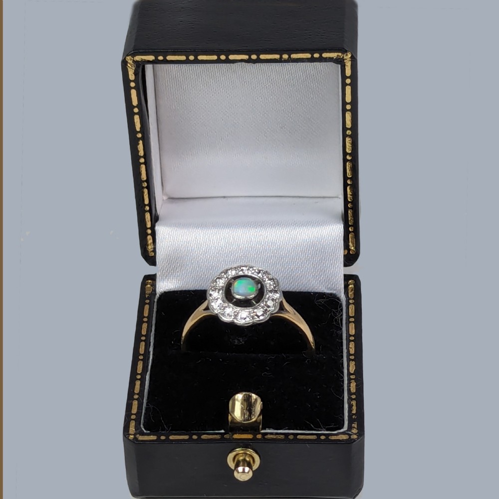 An Edwardian 18ct gold and platinum cluster ring featuring a central cabochon opal surrounded by a halo of diamonds. View VI