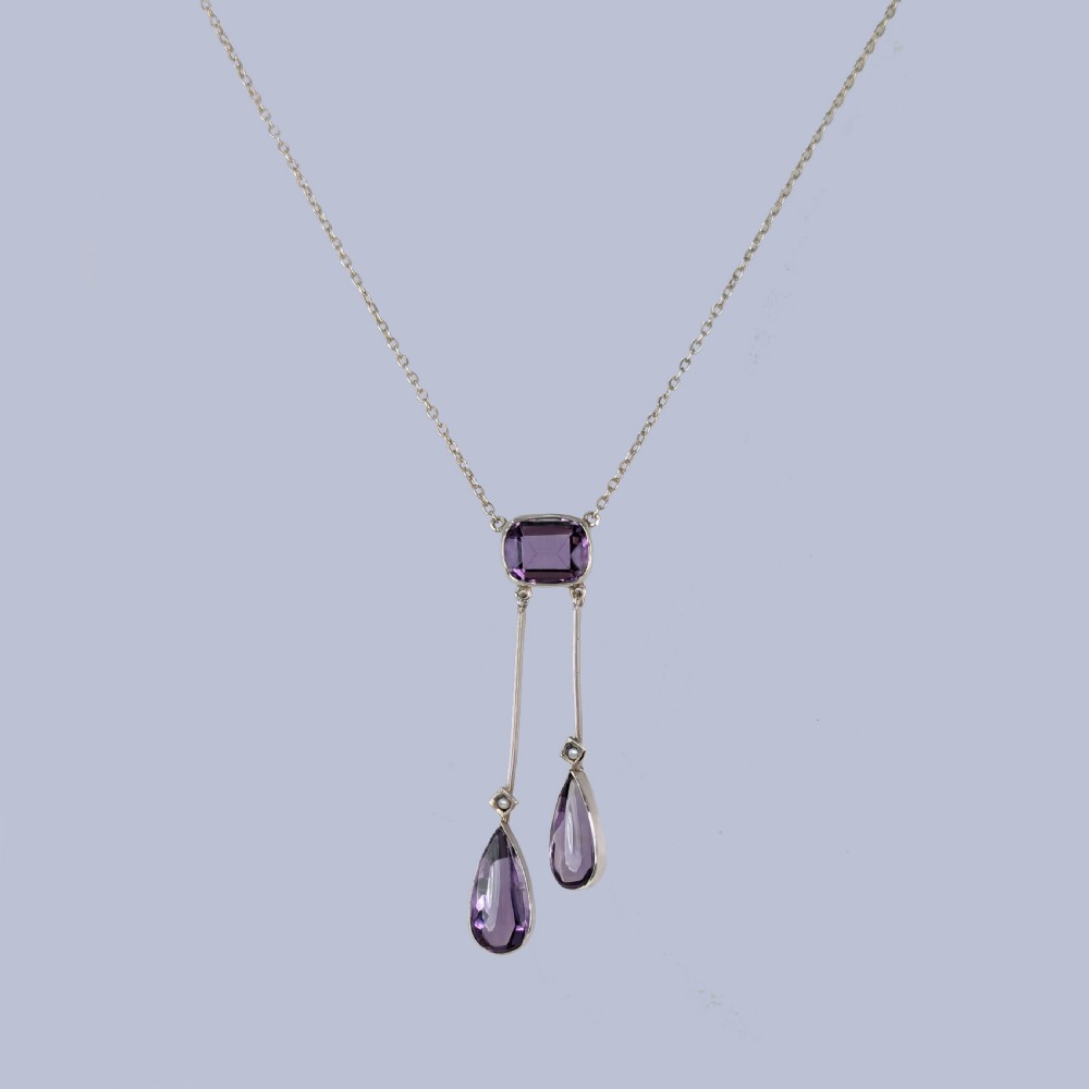 An Edwardian gold negligee necklace displaying a central cushion-cut amethyst suspending two asymmetrical vertical drops with pear-cut amethysts and seed pearls. View V