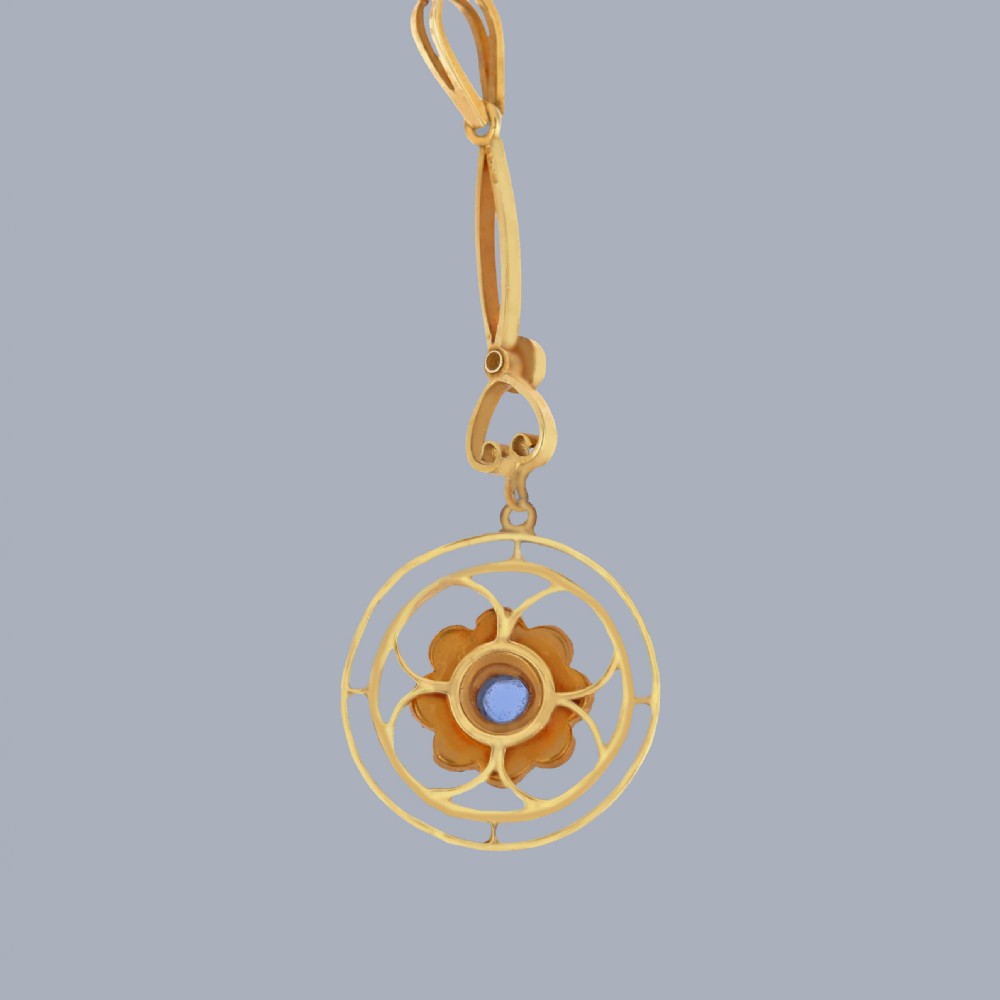 An Edwardian 15ct gold drop pendant featuring a central round blue sapphire surrounded by seed pearls within an openwork circular frame. View VII