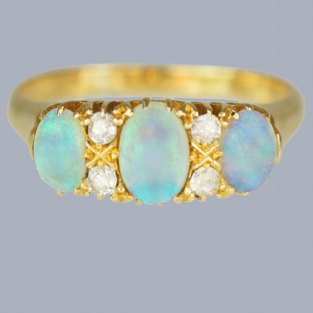An antique 18ct yellow gold ring featuring three oval cabochon opals set horizontally with four small round diamonds placed between them.