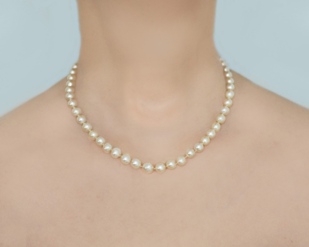 A single strand of cream-coloured pearls hand-knotted on silk thread resting neatly around a neck. View VIII