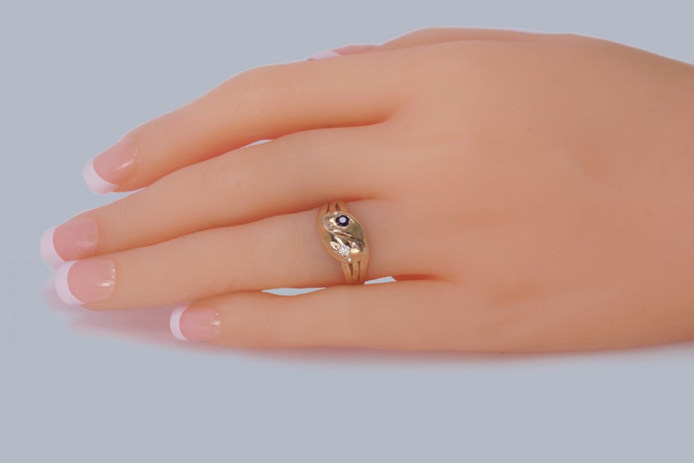 An 18ct yellow gold Edwardian double serpent ring featuring entwined snake heads set with a round blue sapphire and diamonds. View IX