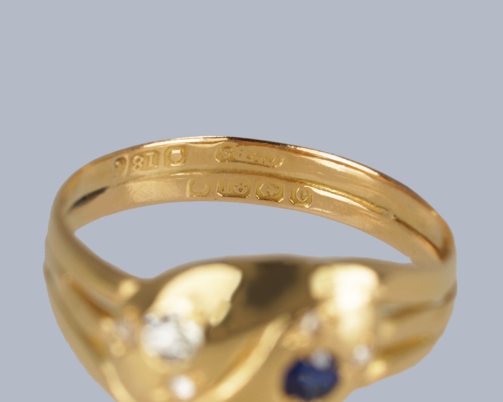 An 18ct yellow gold Edwardian double serpent ring featuring entwined snake heads set with a round blue sapphire and diamonds. View X
