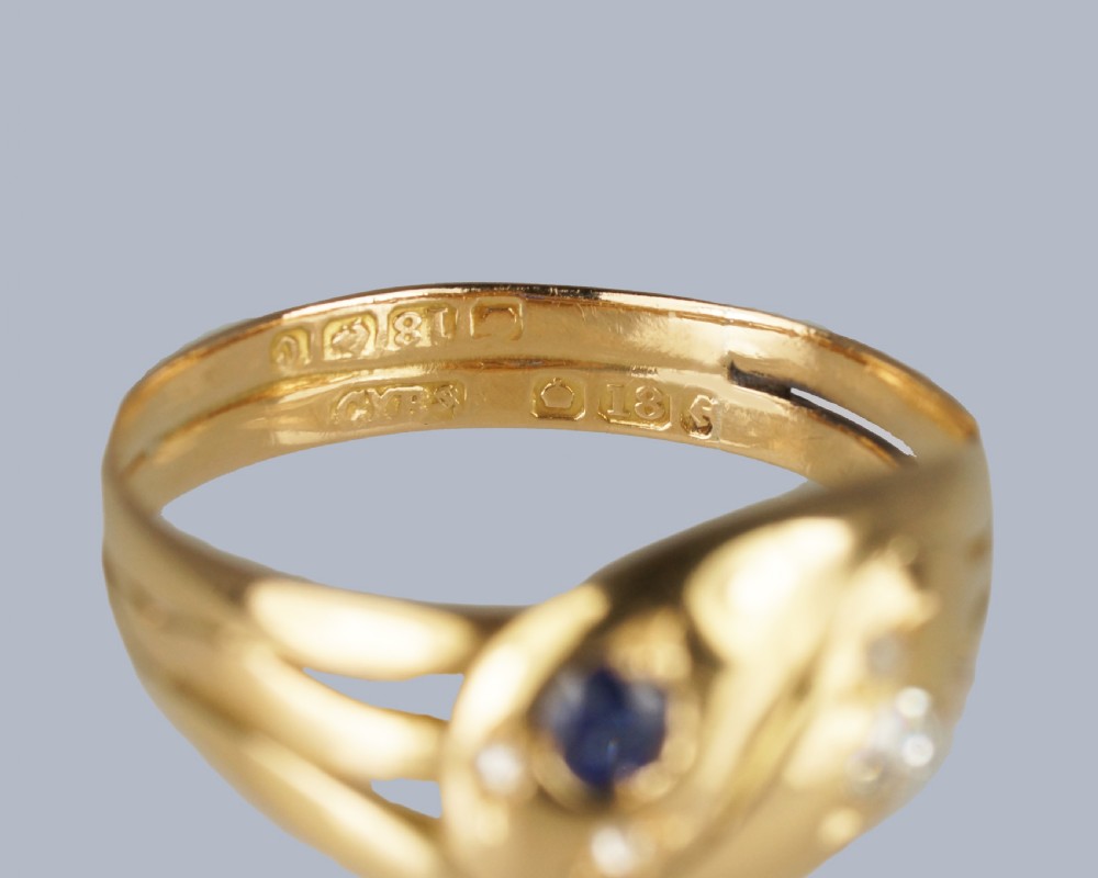 An 18ct yellow gold Edwardian double serpent ring featuring entwined snake heads set with a round blue sapphire and diamonds. View XI