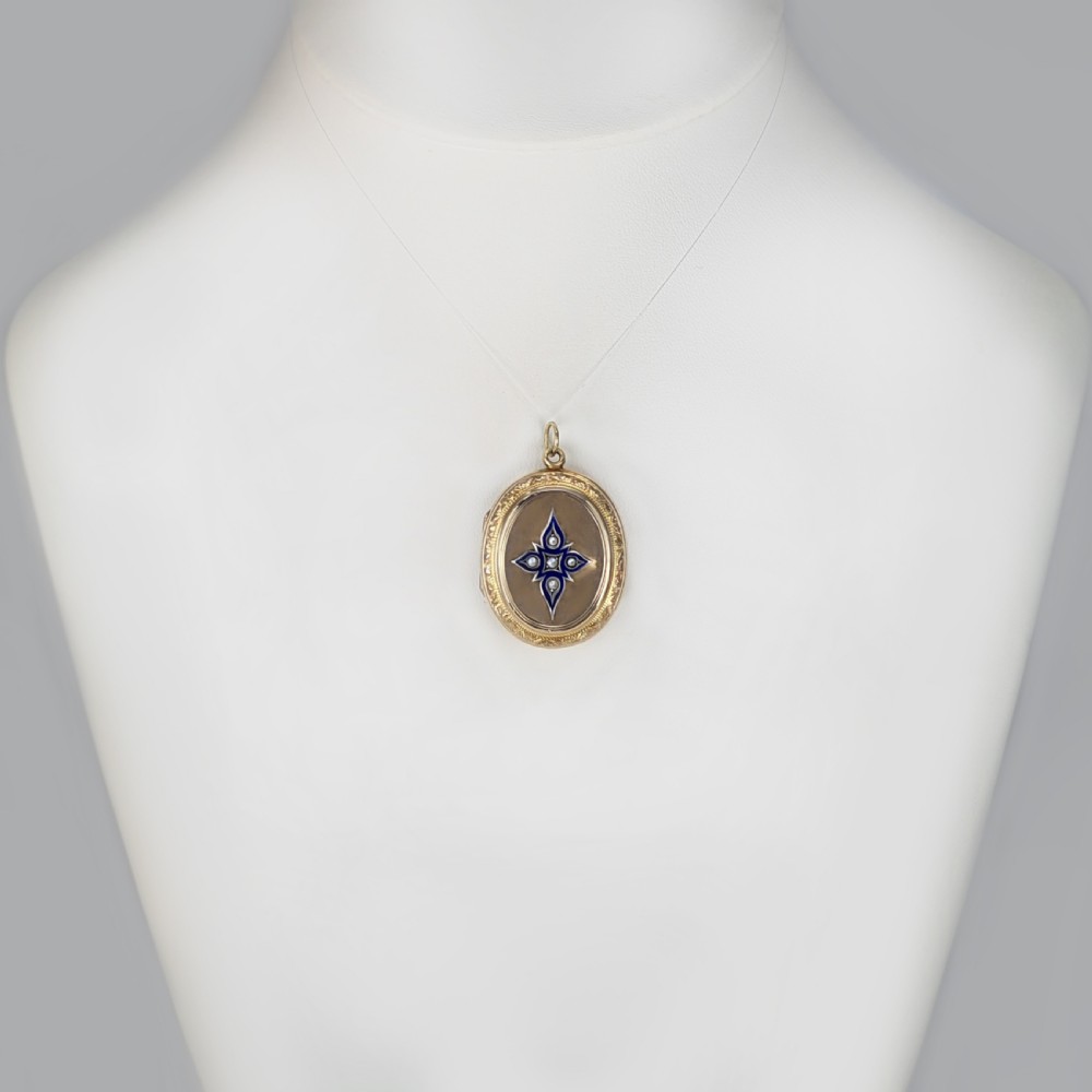 An oval yellow gold Victorian locket featuring a central blue enamel star set with seed pearls and surrounded by an engraved foliate border. View VIII