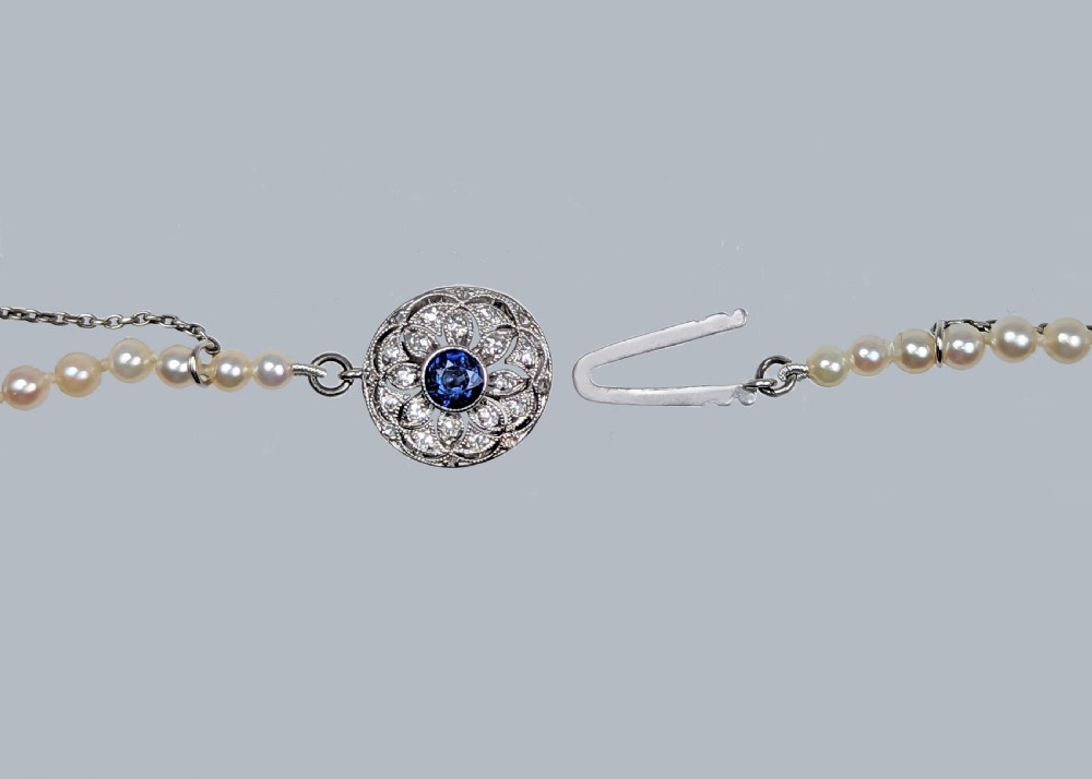 A single strand of cream cultured pearls featuring a circular floral clasp set with a central blue sapphire and surrounding diamonds. View VII