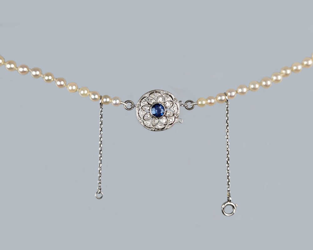A single strand of cream cultured pearls featuring a circular floral clasp set with a central blue sapphire and surrounding diamonds. View VIII