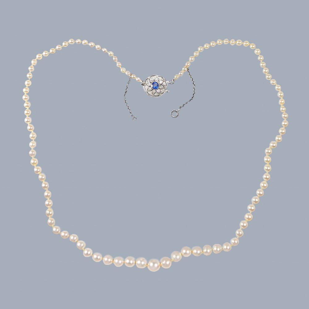 A single strand of cream cultured pearls featuring a circular floral clasp set with a central blue sapphire and surrounding diamonds.