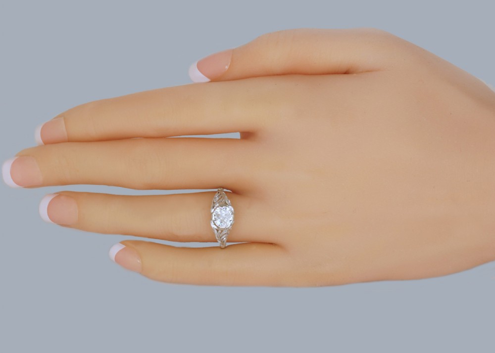 A top-down view of an Edwardian platinum solitaire ring featuring a central old cut diamond set in carved pierced shoulders. View II