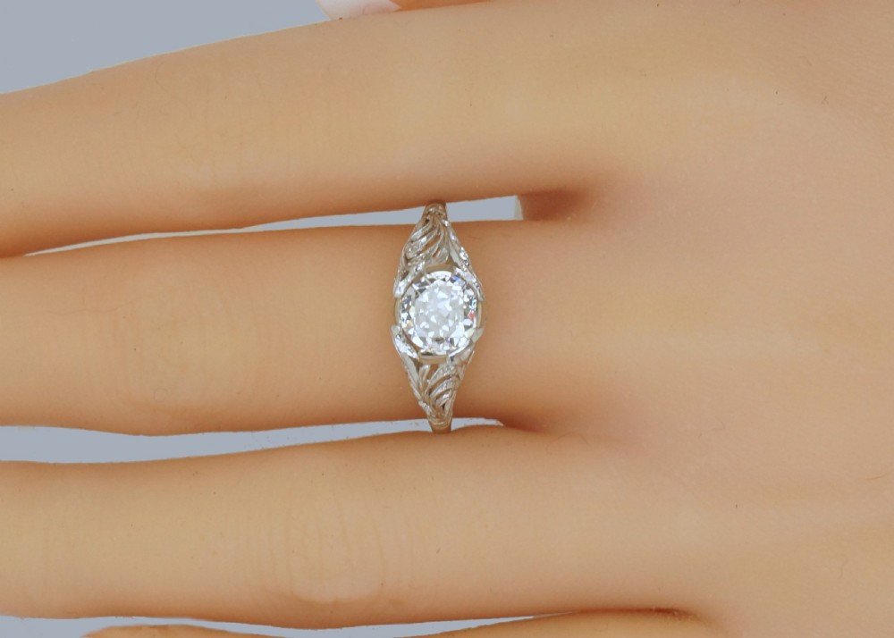 A top-down view of an Edwardian platinum solitaire ring featuring a central old cut diamond set in carved pierced shoulders. View IV