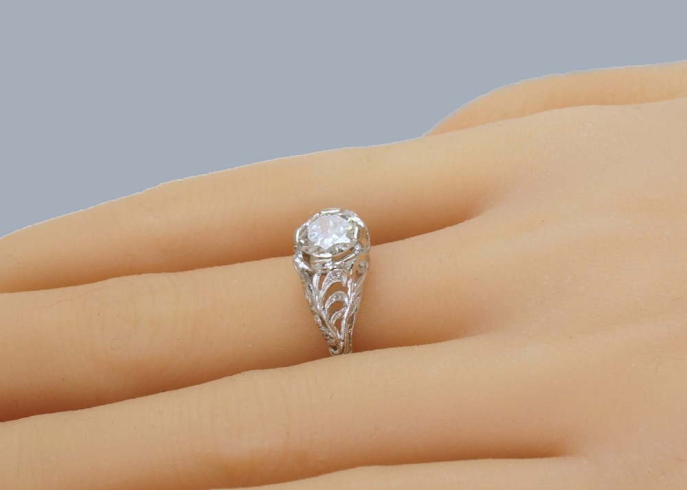 A top-down view of an Edwardian platinum solitaire ring featuring a central old cut diamond set in carved pierced shoulders. View VII