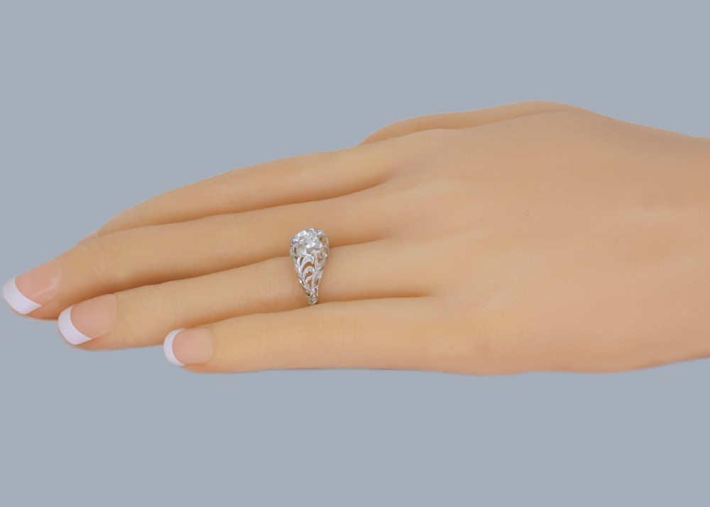 A top-down view of an Edwardian platinum solitaire ring featuring a central old cut diamond set in carved pierced shoulders. View VIII