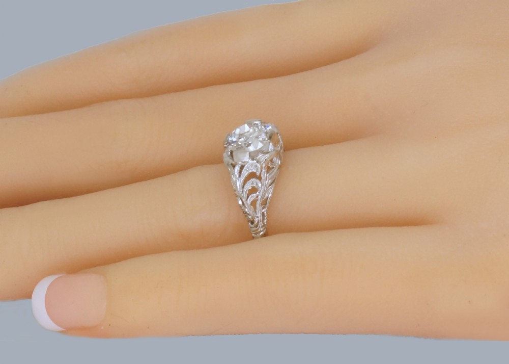 A top-down view of an Edwardian platinum solitaire ring featuring a central old cut diamond set in carved pierced shoulders. View IX