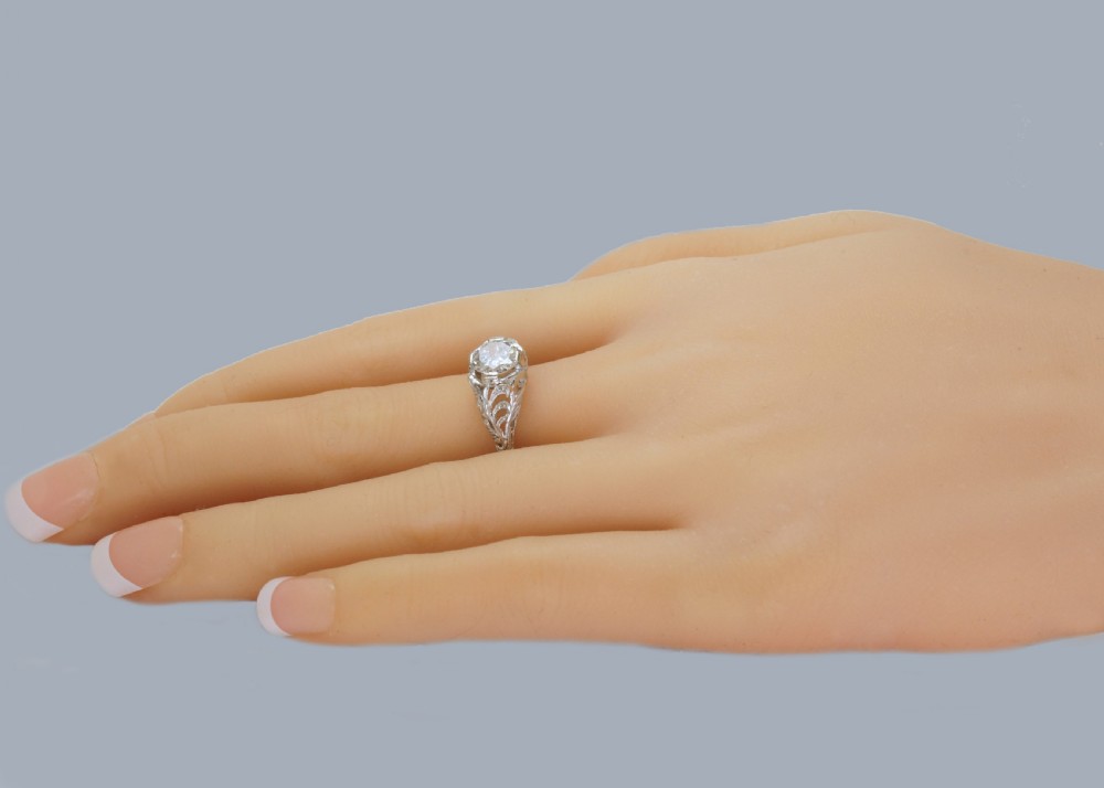A top-down view of an Edwardian platinum solitaire ring featuring a central old cut diamond set in carved pierced shoulders. View XV