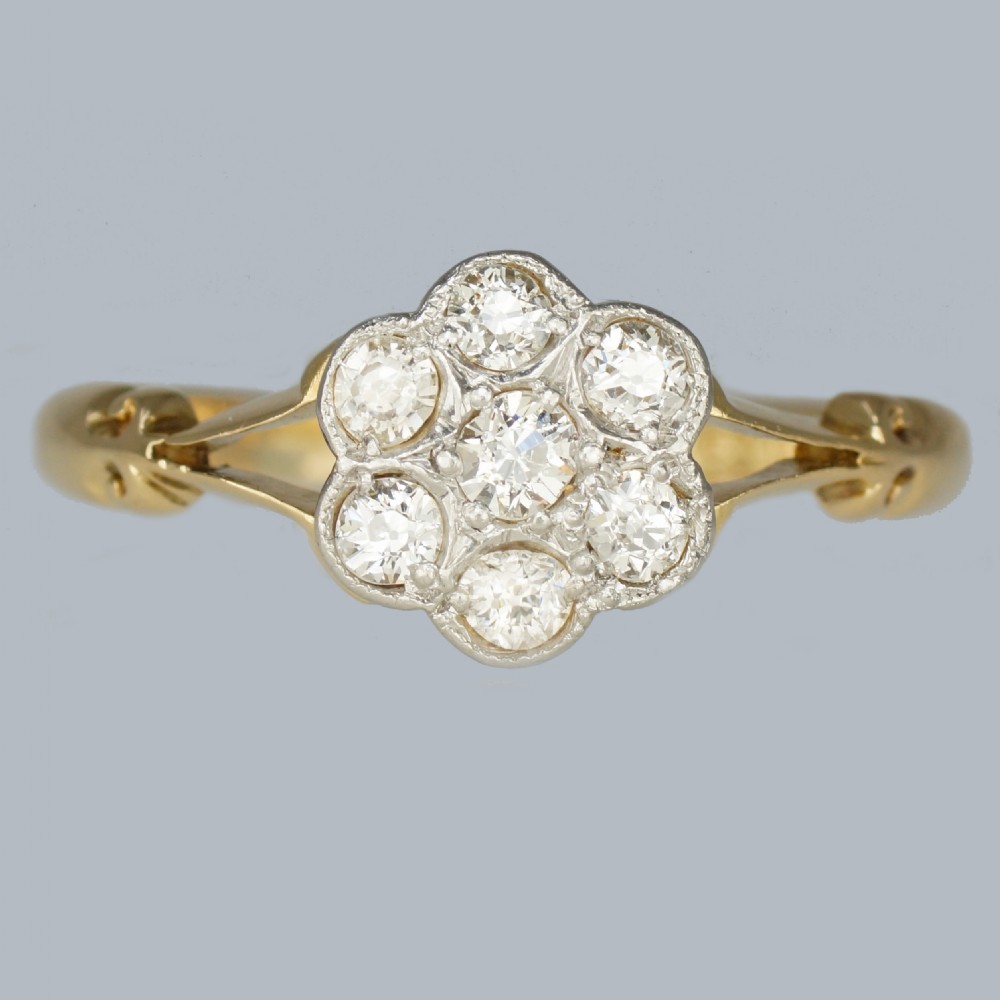 An antique 18ct yellow gold ring featuring a seven-stone diamond cluster set in a flower shape on split scrolled shoulders.