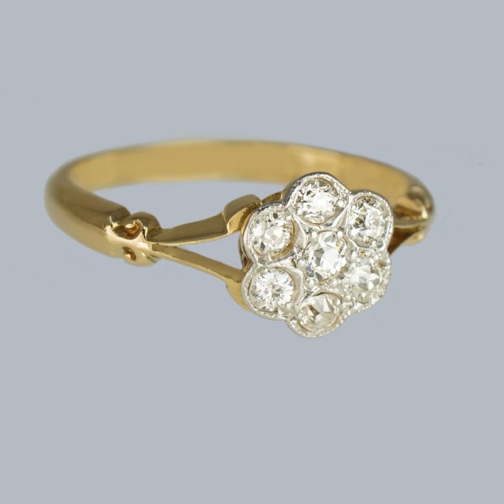 An antique 18ct yellow gold ring featuring a seven-stone diamond cluster set in a flower shape on split scrolled shoulders. View IV
