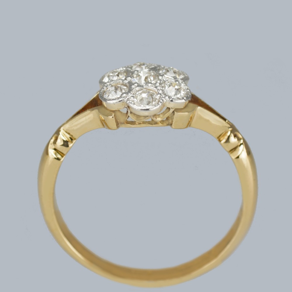An antique 18ct yellow gold ring featuring a seven-stone diamond cluster set in a flower shape on split scrolled shoulders. View V