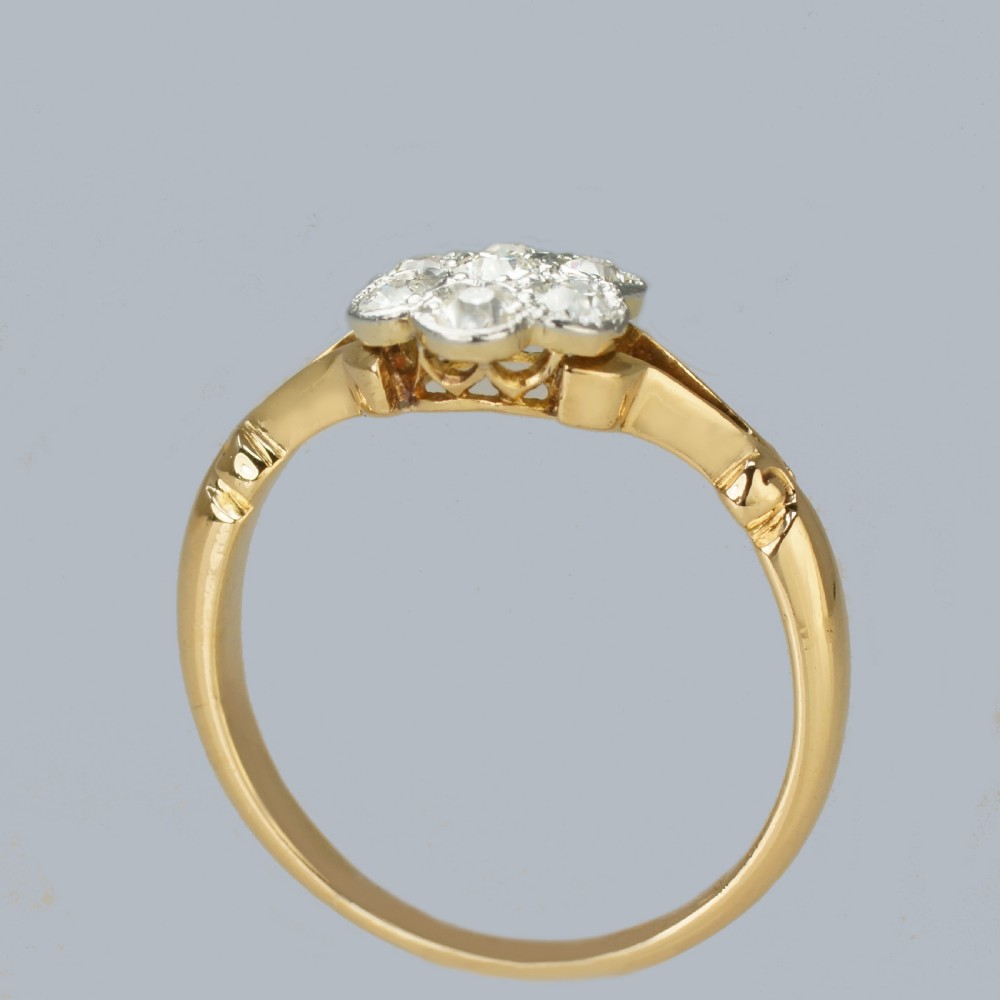 An antique 18ct yellow gold ring featuring a seven-stone diamond cluster set in a flower shape on split scrolled shoulders. View VI