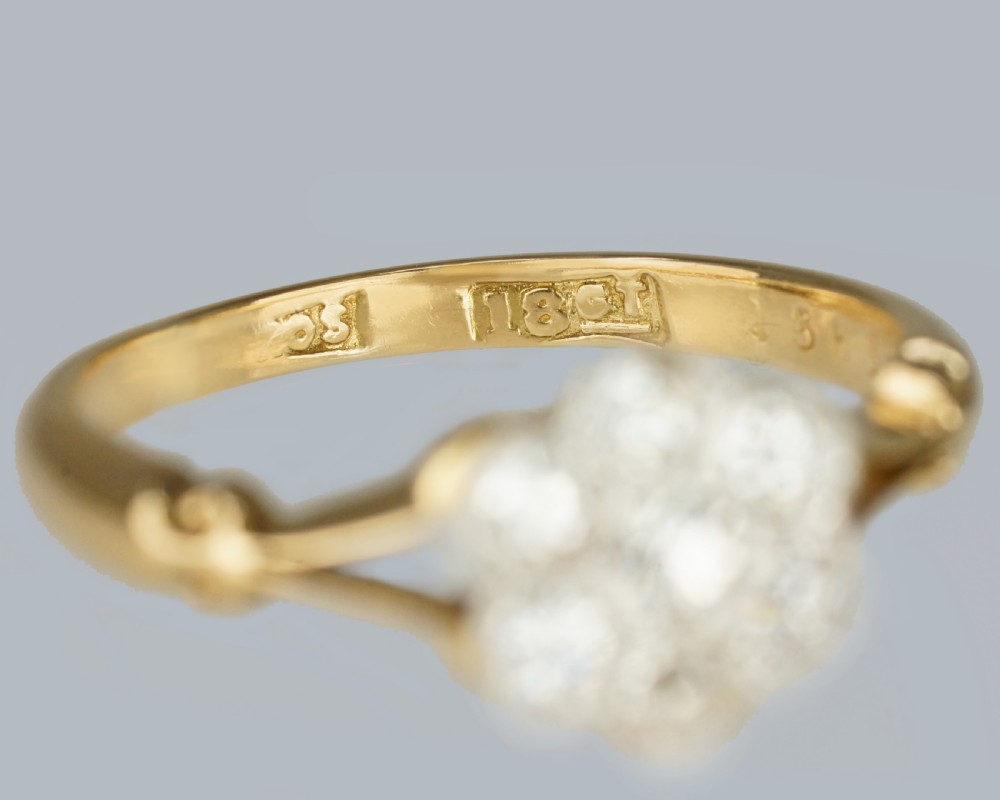 An antique 18ct yellow gold ring featuring a seven-stone diamond cluster set in a flower shape on split scrolled shoulders. View VII