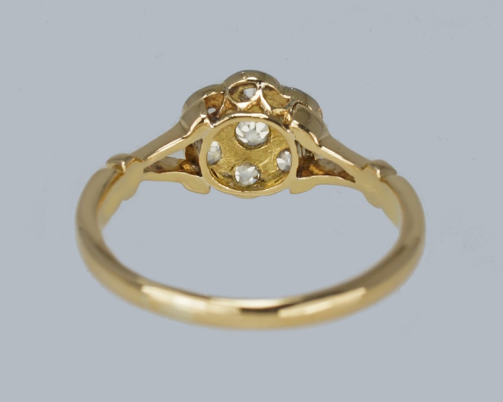 An antique 18ct yellow gold ring featuring a seven-stone diamond cluster set in a flower shape on split scrolled shoulders. View VIII