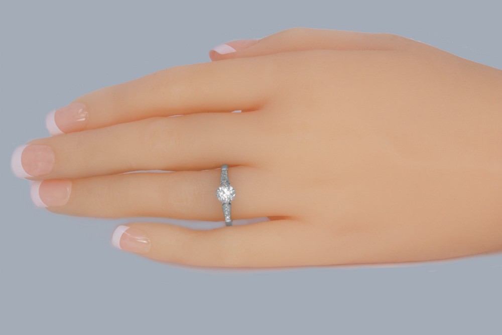 An Art Deco diamond solitaire ring featuring a round central diamond flanked by geometric shoulders set with small accent diamonds in white gold and platinum. View II