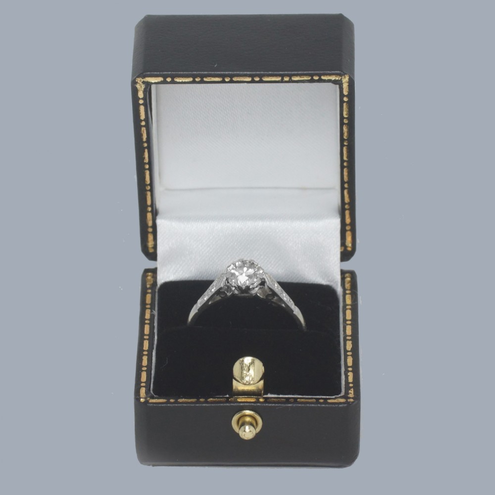 An Art Deco diamond solitaire ring featuring a round central diamond flanked by geometric shoulders set with small accent diamonds in white gold and platinum. View XI