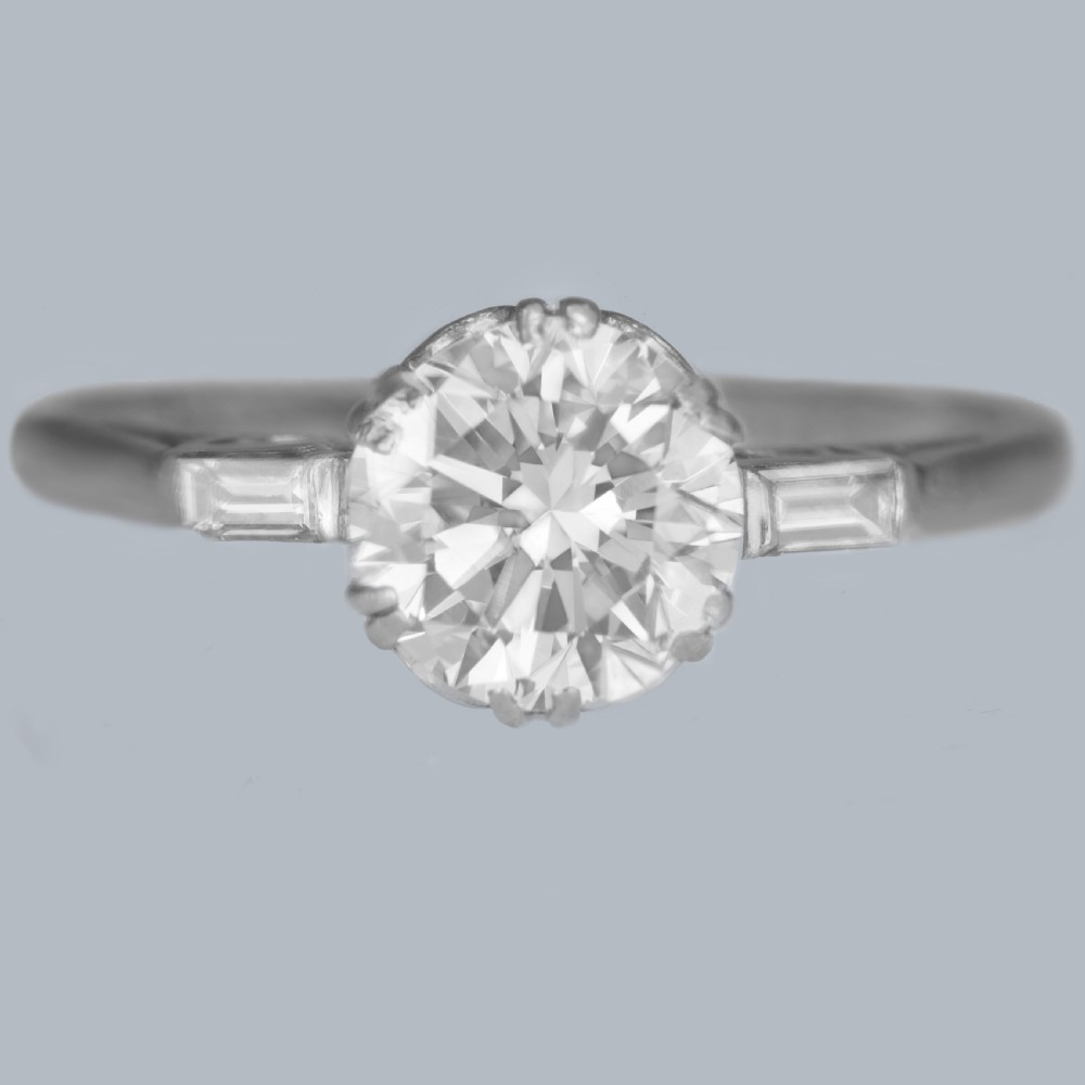 An Art Deco platinum solitaire ring featuring a round brilliant cut diamond flanked by stepped baguette cut shoulder stones.