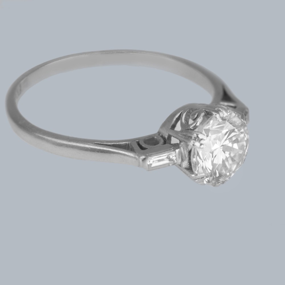 An Art Deco platinum solitaire ring featuring a round brilliant cut diamond flanked by stepped baguette cut shoulder stones. View V