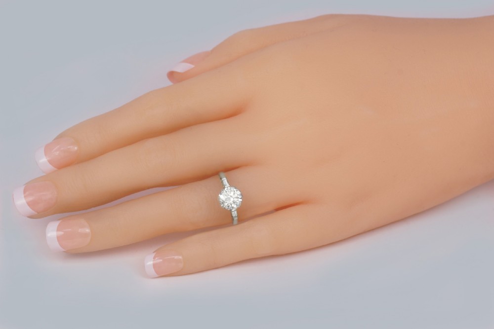 An Art Deco platinum solitaire ring featuring a round brilliant cut diamond flanked by stepped baguette cut shoulder stones. View VII