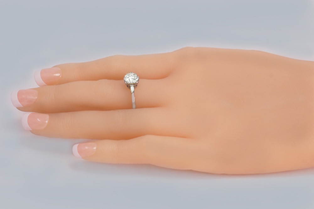 An Art Deco platinum solitaire ring featuring a round brilliant cut diamond flanked by stepped baguette cut shoulder stones. View VIII